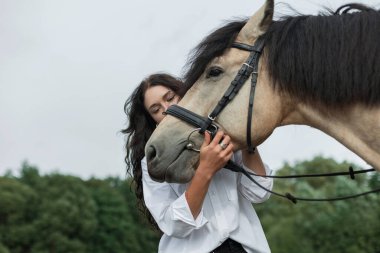Kırsal kesimde, yaz sahasında bir atı nazikçe kucaklayan zarif bir kadın. Kırsal alanda atı olan genç bir kadın binicilik bağı, güven kırsal yaşam tarzı ve doğa bağlantısını gösteriyor.