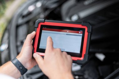 Araç kabininde, elektronik sistemleri ve motor performansını kontrol eden bir araç tanılama tarayıcısı tutan kişi. Otomotiv teknolojisi ve onarım kavramı.