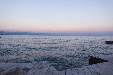 Hırvatistan 'da Adriyatik Denizi kıyısında gün batımında huzurlu bir deniz manzarası. Sakin deniz kenarında tahta bir güverte ile yaz tatili sahnesini rahatlatıyor. Deniz kenarında bir akşam