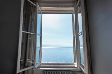 Sakin mavi deniz ve açık gökyüzü manzaralı açık bir pencere. Rahatlamayı, özgürlüğü, seyahati ve okyanus kıyısındaki huzurlu yaz tatilini simgeliyor..