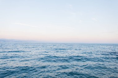 Gün batımında berrak bir gökyüzünün altında, sakin, mavi dalgalı bir deniz. Asgari deniz manzarası barış, özgürlük ve sükuneti simgeliyor. Seyahat, doğa ve rahatlama kavramları için mükemmel..