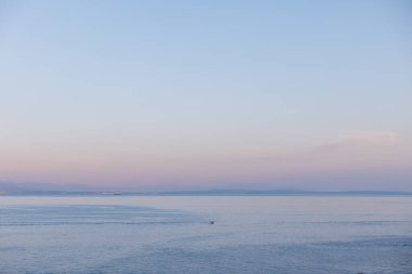 Hırvatistan 'ın Opatija kentinin manzaralı deniz manzarası, Adriyatik Denizi kıyısında uzak tepeler ve sakin su. Hırvatistan 'daki Opatija kıyı şeridi, şehir silueti ve gün batımında dağ zeminiyle sakin deniz ufku