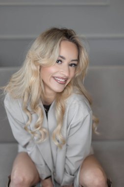 Göz kamaştırıcı genç flama sarışın kız evdeki kanepede oturuyor. Moda güzeli bayan.