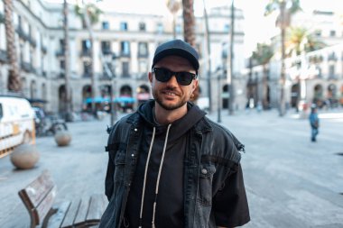 Şehirde Barselona 'da siyah kot elbiseli, şapkalı, güneş gözlüklü havalı, yakışıklı bir adam yürüyor.