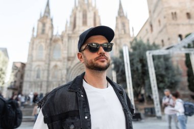 Siyah şapkalı, modaya uygun giyinen, modaya uygun bir adam Barcelona 'da kilise yakınlarında yürüyor.