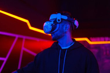 Yakışıklı adam, neon ışıklı sanal gerçeklik kulaklığı kullanıyor. VR, gelecek, cihazlar, teknoloji, eğitim çevrimiçi, öğrenim, video oyunu konsepti