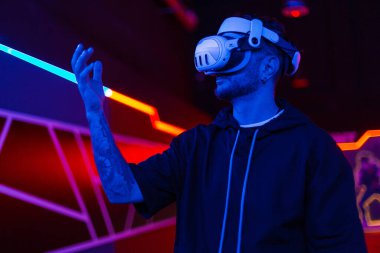 Sanal gerçeklik gözlüklü sakallı genç adam stüdyoda mavi ve pembe ışıklı..