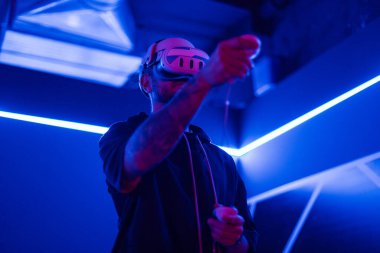 VR gözlüklü havalı adam neon ışıkta joysticklerle oyun oynuyor. Metaverse, sanal gerçeklik gözlükleri ve VR kontrollü fütüristik oyun, siber ve 3D dünyası olan bir adam. Oyuncu kişi