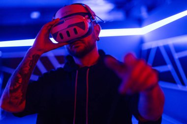 VR gözlüklü havalı moda teknisyeni sanal menüyü kontrol ediyor ve neon ışıklı karanlık odada parmaklarına dokunuyor.
