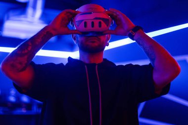 Moda teknisyeni karanlık odada neon ışıklı modern VR gözlükler takıyor. Sanal dünyada oyuncu