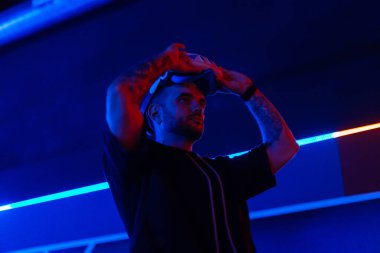 Havalı yakışıklı moda teknisyeni karanlık odada neon ışıklı VR gözlük takıyor. Sanal gerçeklik