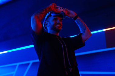 Havalı yakışıklı moda teknisyeni karanlık odada neon ışıklı VR gözlük takıyor. Sanal gerçeklik