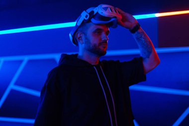 Havalı profesyonel bir adam koyu arkaplanlı, neon mavi ve kırmızı ışıklı sanal gerçeklik gözlüğü takıyor. Gelecek teknolojisi, oyun, eğlence ve insan konsepti - sanal gerçeklik kulaklığı olan mutlu genç adam