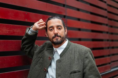 Sokakta kırmızı duvarın yanında duran şık elbiseli yakışıklı bir adam. Havalı moda adamı.