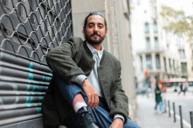 Sakallı ve bıyıklı yakışıklı hippi. Barcelona şehrinin caddesindeki binanın yanında montlu sıradan kıyafetler giyiyor. Şehir adamı.