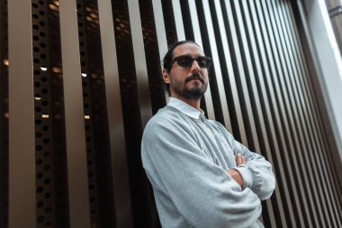 Havalı, yakışıklı, şık güneş gözlüklü, günlük kıyafetler giyen, kazağı ve gömleği sokağın duvarında duran moda adamı.