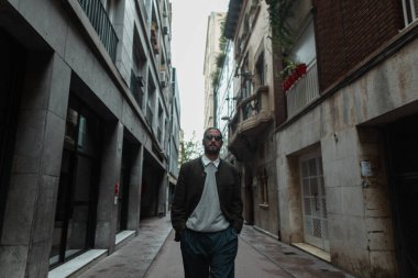 Moda kıyafetleri içinde şık yakışıklı bir adam Barselona 'da binaların yakınında yürürken palto giyiyor.