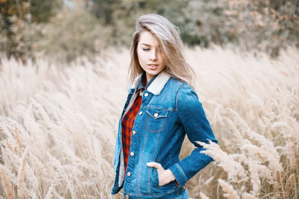 Chica joven en ropa vaquera y una camisa a cuadros rojo en el campo de otoño con hierba — Foto de Stock