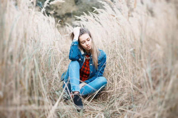 Chica bonita se sienta en una hermosa hierba de otoño. Chaqueta vaqueros azul . — Foto de Stock