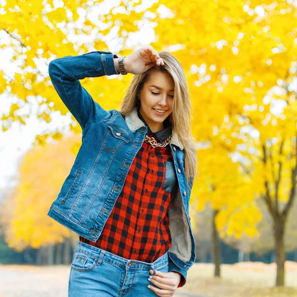 Mujer joven en ropa de mezclilla con hojas de otoño en la mano y el fondo del jardín de arce amarillo otoño — Foto de Stock