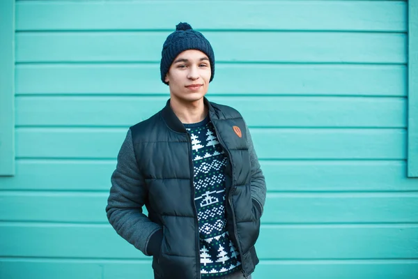 Fiatal jóképű srác egy meleg kötött ruhák hátterében színes fa fal — Stock Fotó