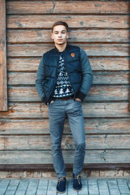 Stylish young man stands against a background of a wooden house.
