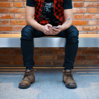 Young stylish man with phone sitting on the bench in a supermarket. Man waiting