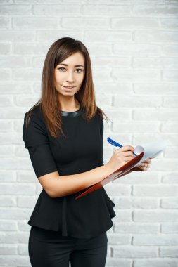 Young girl doing recording, holding pen and notebook.