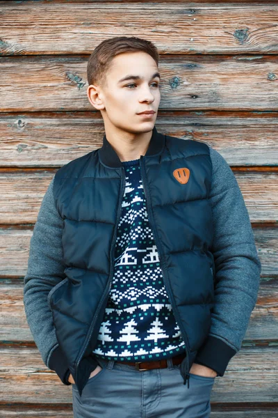 Beau jeune homme en pull tricoté et veste chaude d'hiver près du mur en bois vintage . — Photo