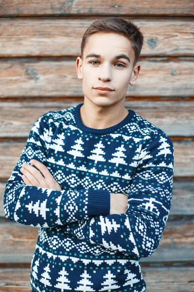 Handsome guy in winter sweater and knit hat on the background of wooden wall. — Stock Fotó