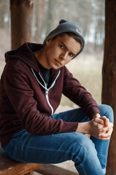 Fiatal férfi sapka és jersey ül egy fa pad az erdőben — Stock Fotó
