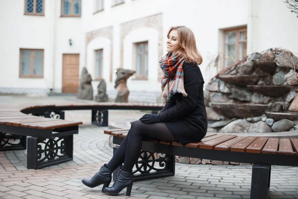Bir eşarp ve siyah ceket binanın arka plan üzerinde bir bankta oturan genç şık kız — Stok fotoğraf