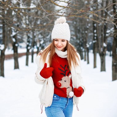 Lovely girl with a stylish retro sweater, a white winter jacket and knit cap looking down on the background of the park