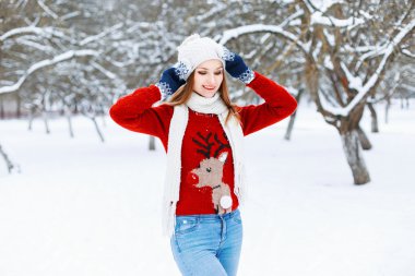 Pretty Woman in red knitted sweater with a deer standing in a winter park.
