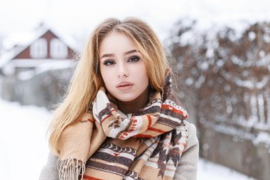 Close-up portrait of a young beautiful girl with winter vintage scarf on the background of the village