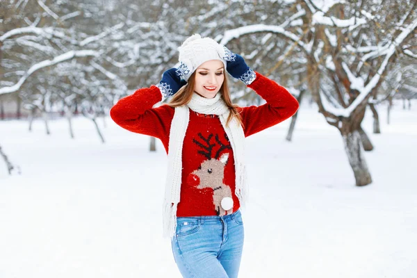 Красотка в красном вязаном свитере с оленем, стоящим в зимнем парке . — стоковое фото