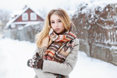 Beautiful woman with a vintage scarf and knitted mittens standing in the village near the fence