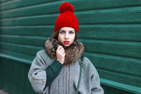 Retro portrait of a beautiful girl in a red hat and coat standing near a green wooden wall — Stok fotoğraf