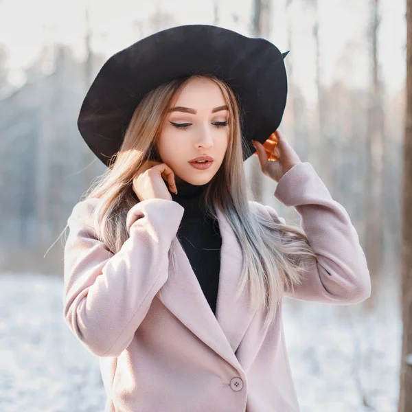 Young beautiful girl in stylish black hat and coat on a background of snowy forest — Zdjęcie stockowe