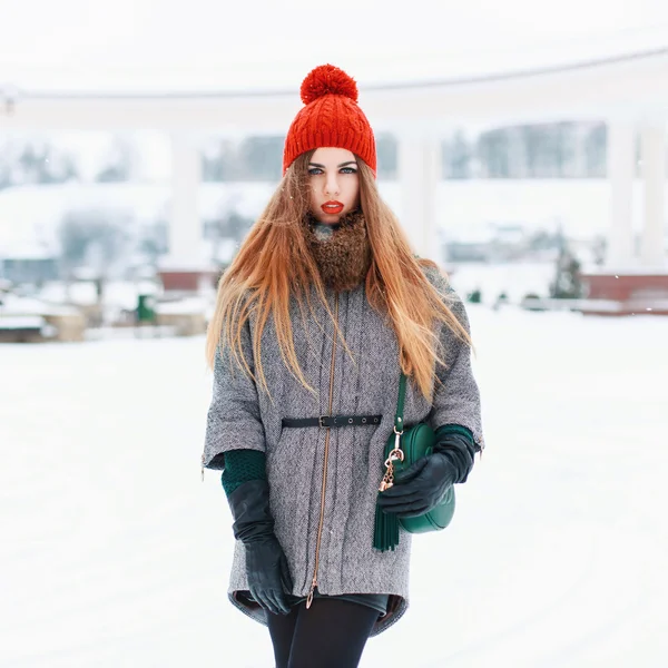 Beautiful woman in a red knit hat and winter coat on a winter background — Stok fotoğraf