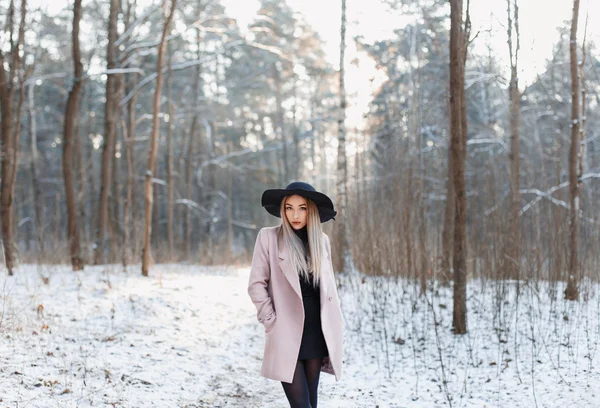 Söt fashionabla kvinna i svart hatt och rosa päls på vintern fantastiska skogen vid solnedgången — Stockfoto