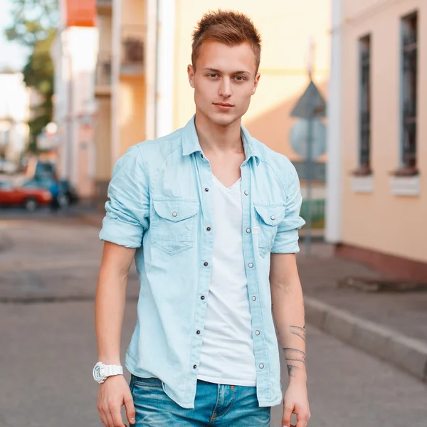 Young handsome man in a denim shirt and jeans on the background of the city. — Stock Photo, Image