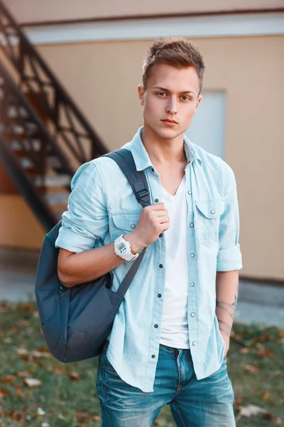 Молодий стильний чоловік в джинсовому одязі з рюкзаком, що йде у дворі — стокове фото