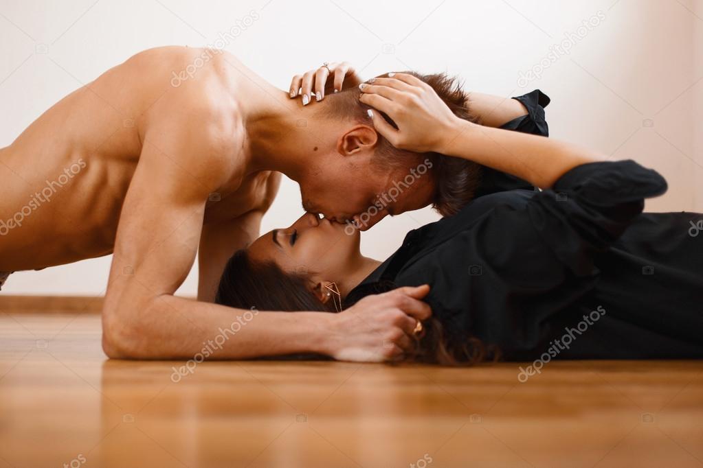 Young beautiful couple kissing on the wooden floor. Handsome man lying over the girl, and kissing