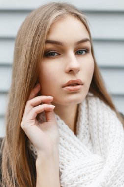 Portrait of a beautiful young woman in a knitted scarf on the background of wooden wall
