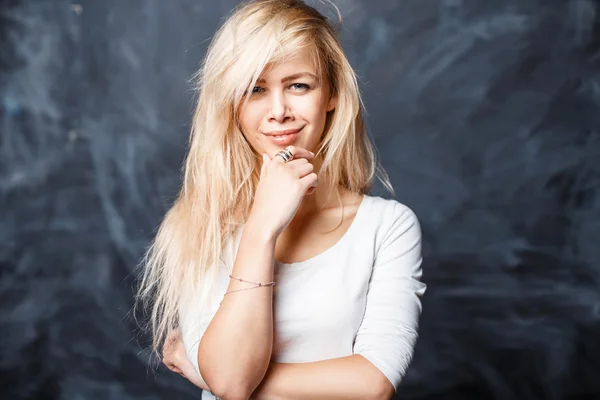 Menina loira bonita em uma camisa branca sorrindo contra um fundo escuro com manchas — Fotografia de Stock