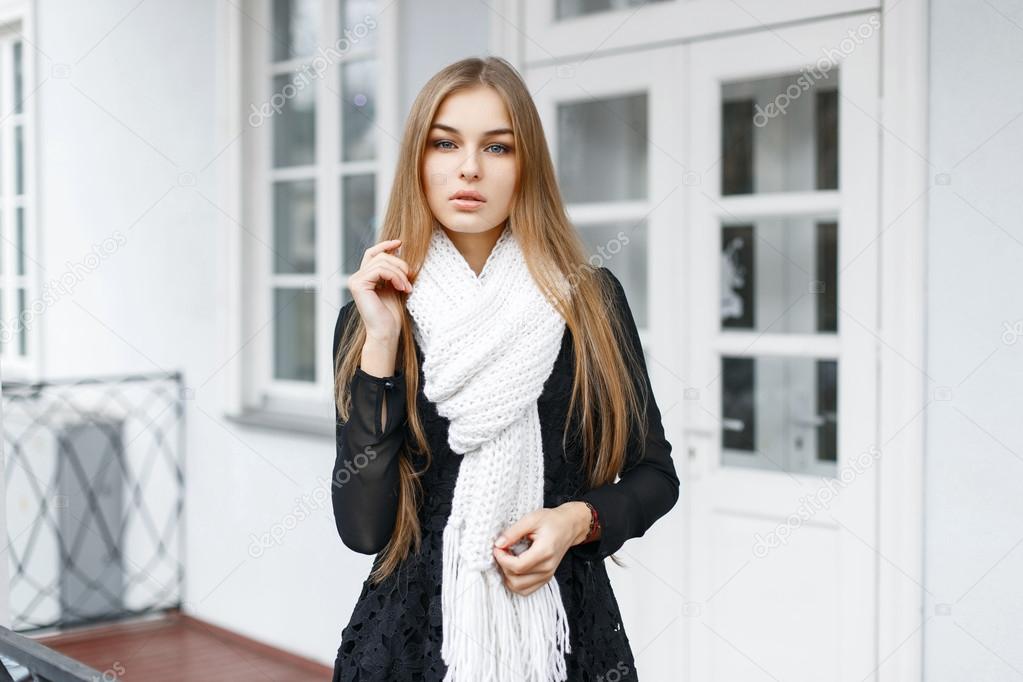 Stylish young beautiful girl in a black dress and a white knitted