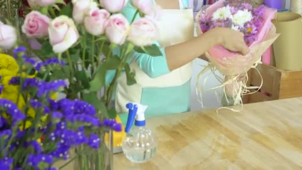 Цветочный магазин, флорист, раскладывающий розовый и белый букет мамы, распыляющий воду на букет — стоковое видео