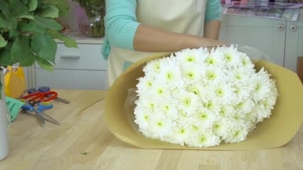 Loja de flores, arranjando buquê de flores, florista envolvendo papel de embrulho marrom em torno do buquê de mães brancas — Vídeo de Stock