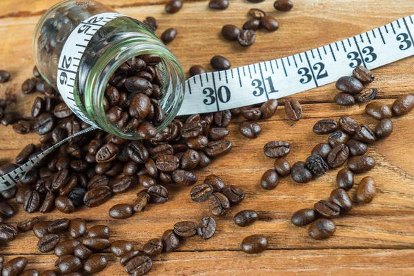 Coffee bean in glass bottle with tape measure on wooden backgrou — Stock Photo, Image